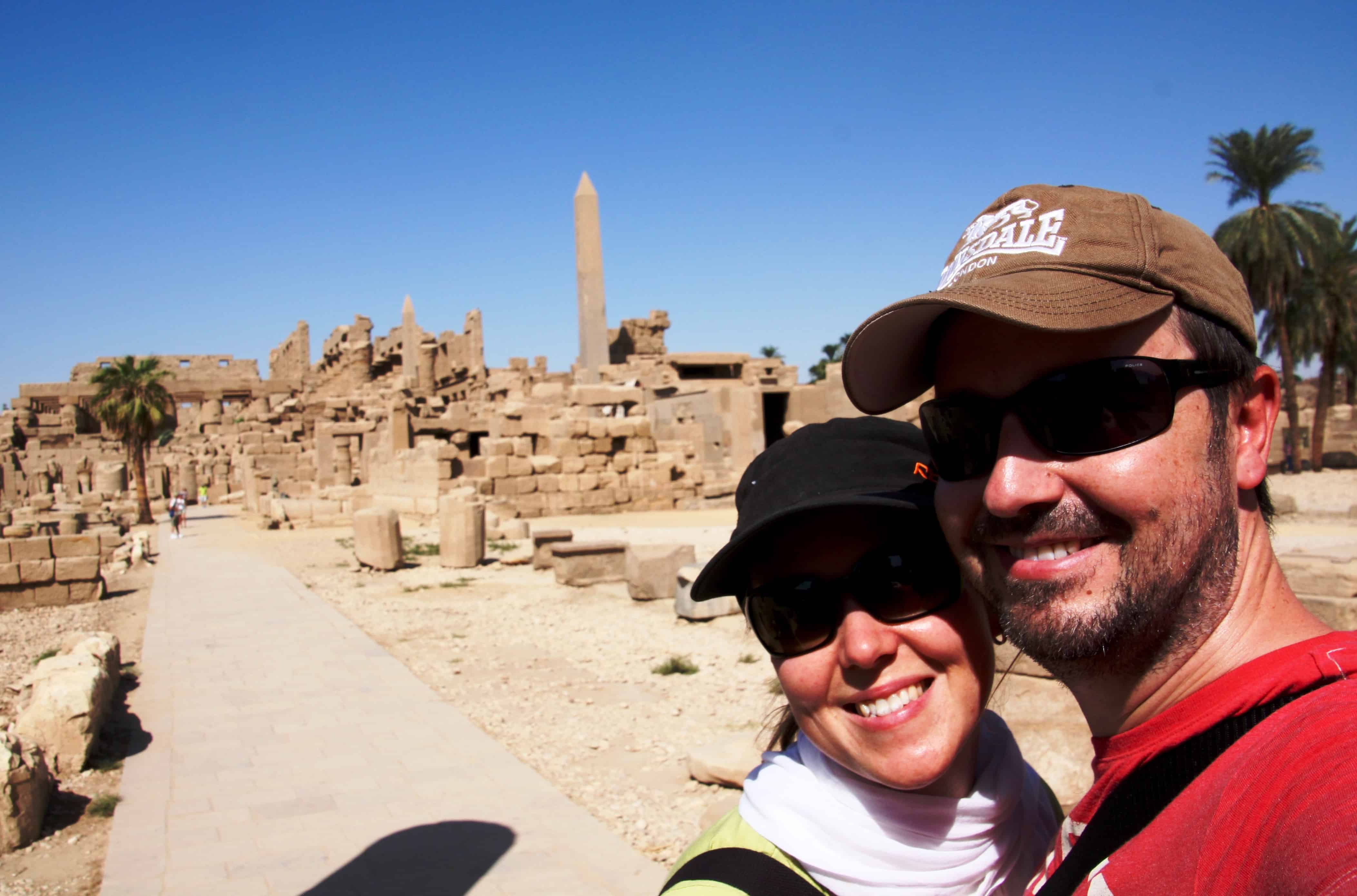 Couple smiles in front of the ruins of the great Temples of Karnak in Egypt.