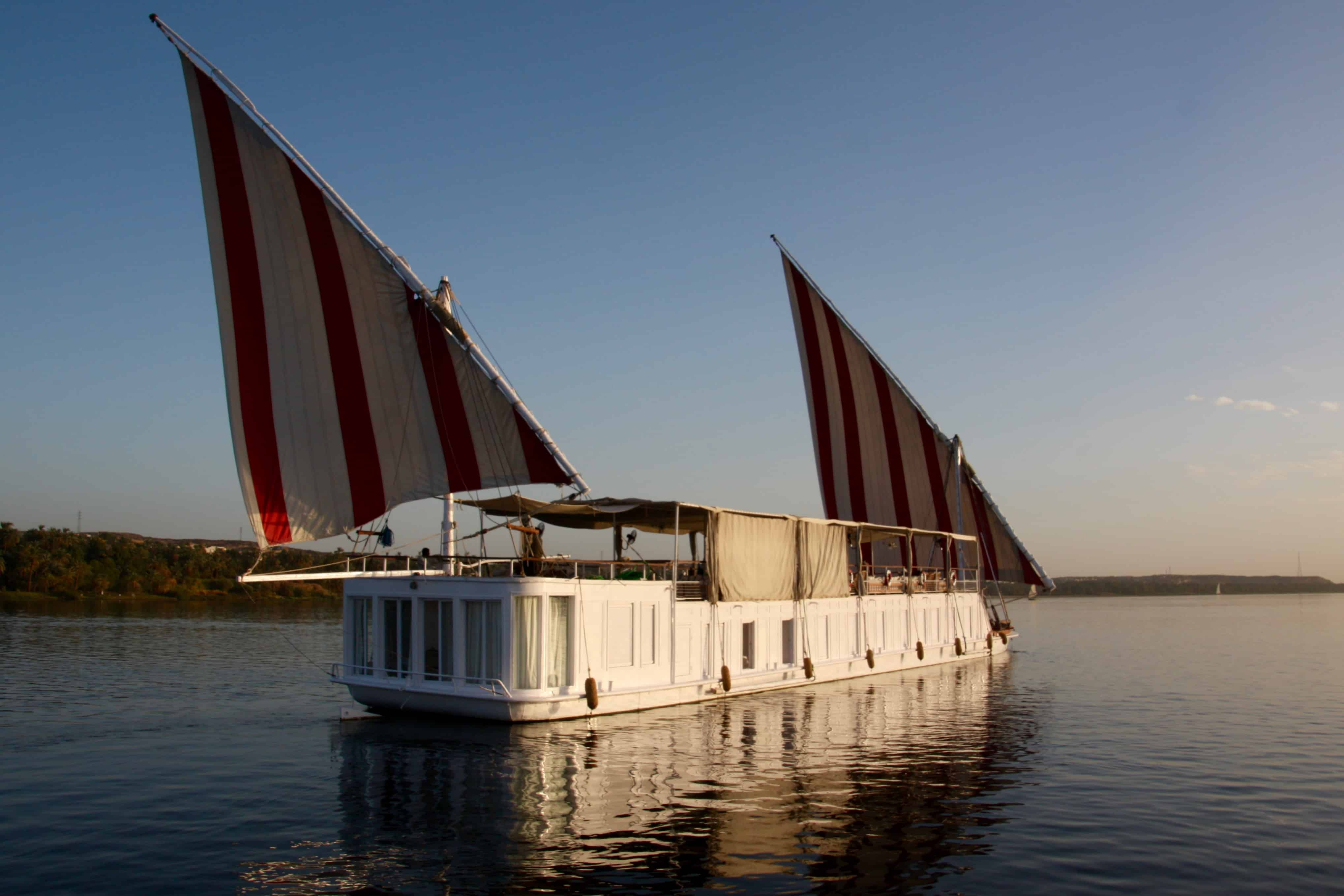 Red and white sails fill with the wind on a traditional dahabiya sailing boat in Egypt. 