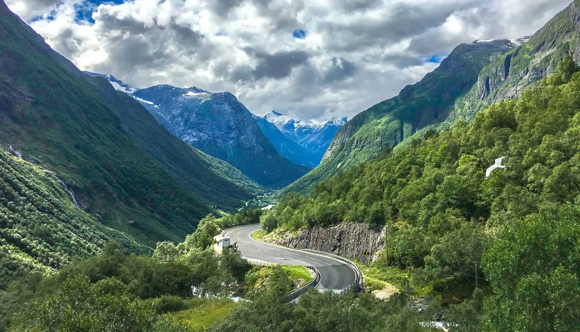 The road winds through lush green mountains on the way to Geiranger on our Norway roadtrip.