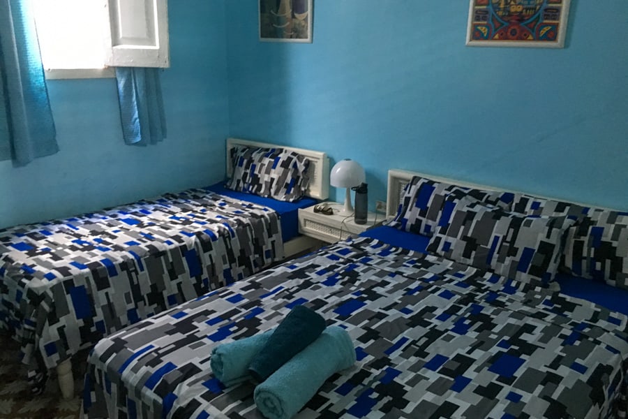 Room with two beds with blue and grey covers and blue walls in an accommodation in Cuba.