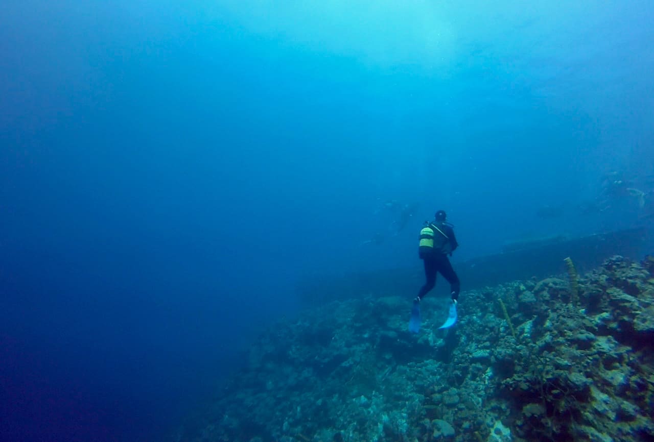 A diver swims near a wreck on the edge of a drop in the Bay of Pigs