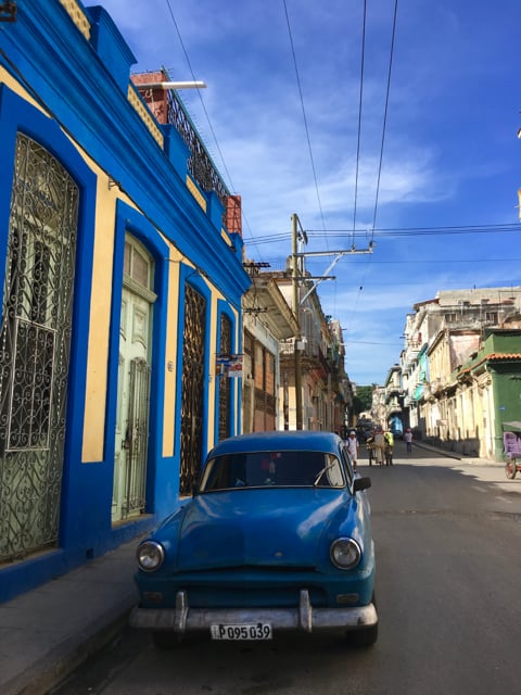 A bright blue vintage car parked by a building of the same colour in Havana, Cuba.