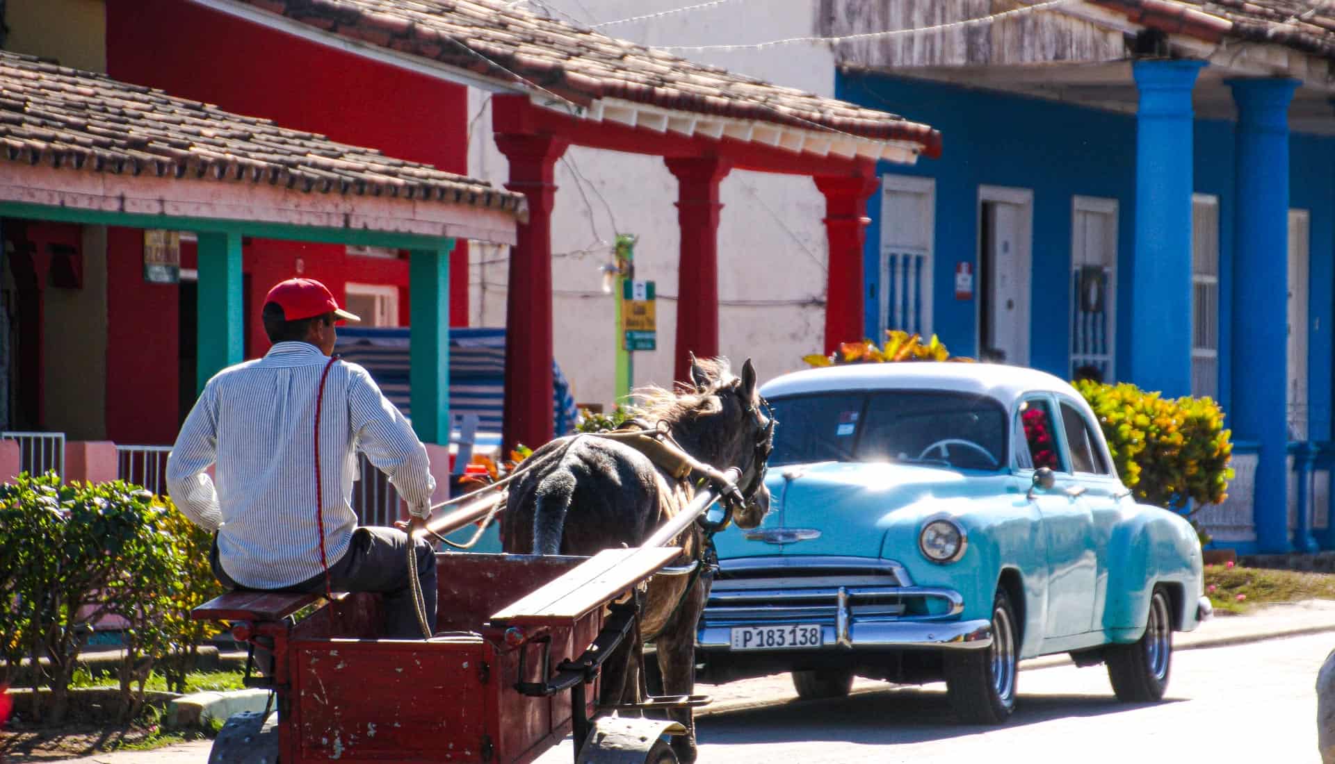 A horsecart passes a vintage car on the streets of Viñales, a typical sight on a Cuba itinerary.