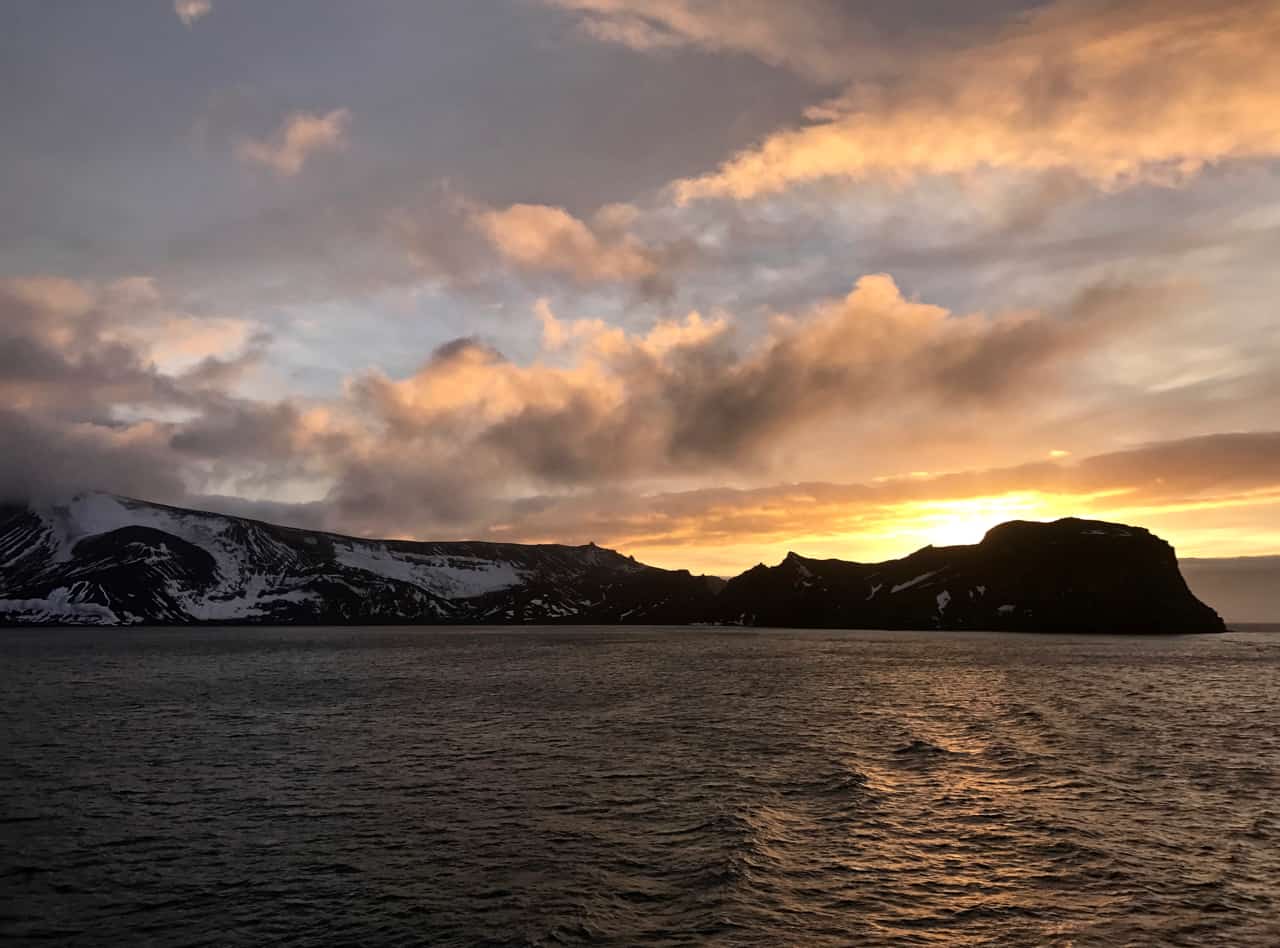 The sun rises behind the black silhouetted rocks at the entrance to Deception Bay in Antarctica.