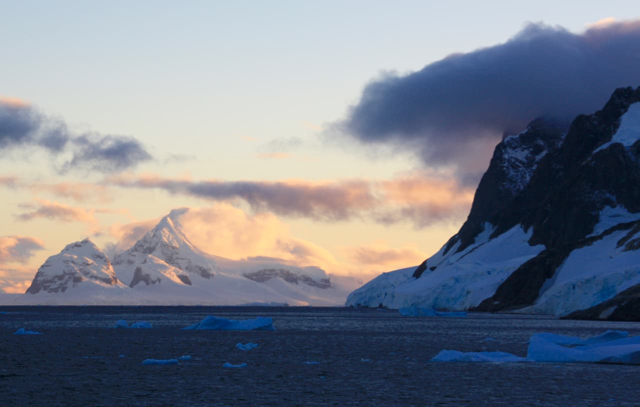 Dawn turns a snow-covered mountain golden while another mountain sits in shadow in Antarctica.