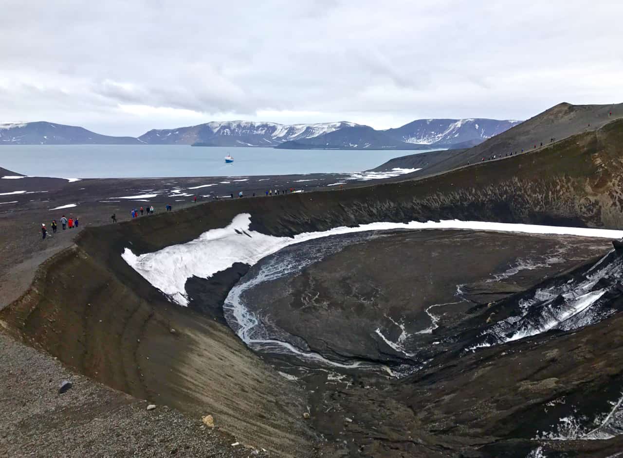 A black volcanic crater edged with ice dominates the view over Telefon Bay at Deception Island in Antarctica.
