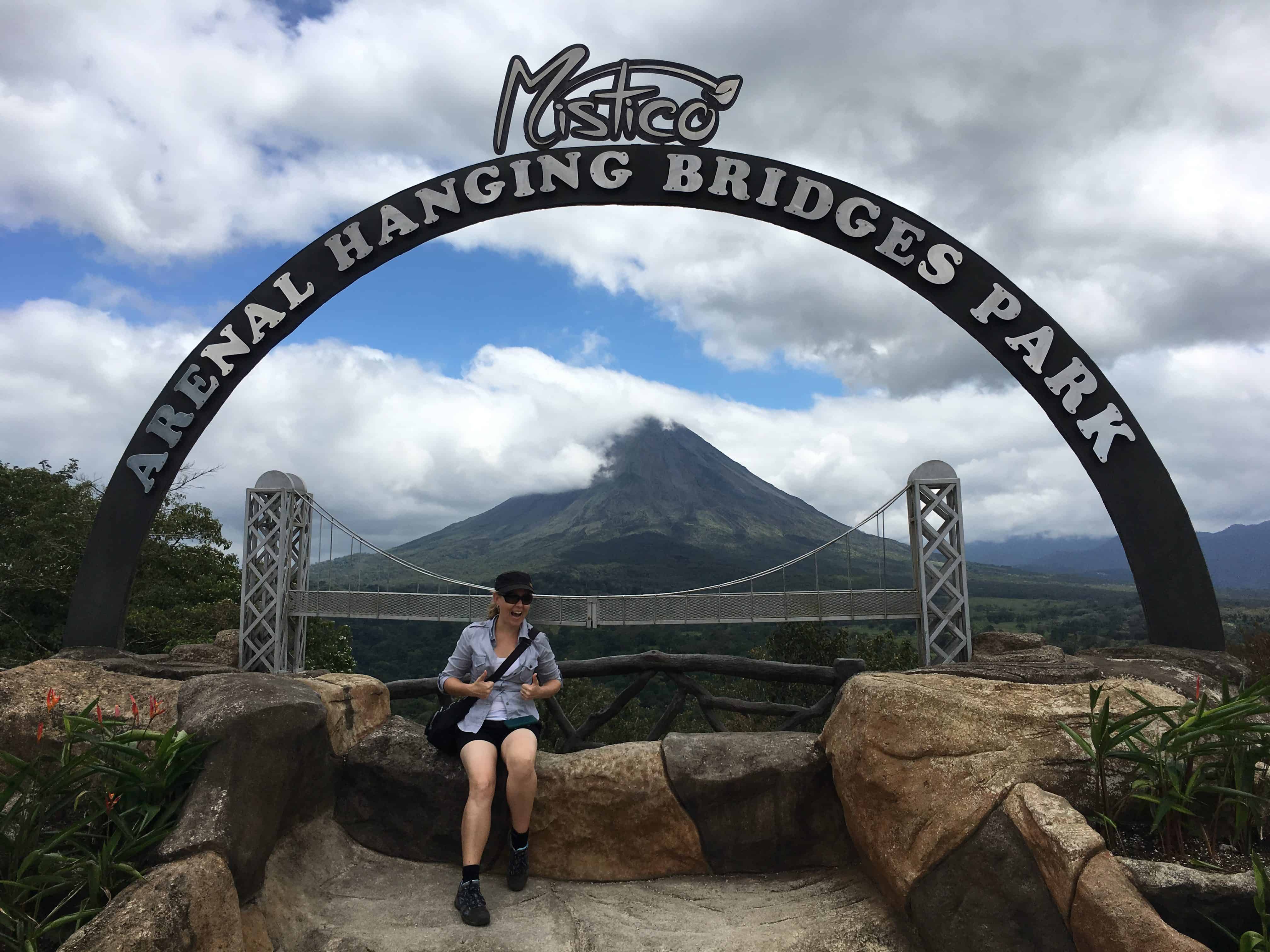  Dan si trova sotto un arco a Mistico Hanging Bridges Park con il vulcano Arenal sullo sfondo.