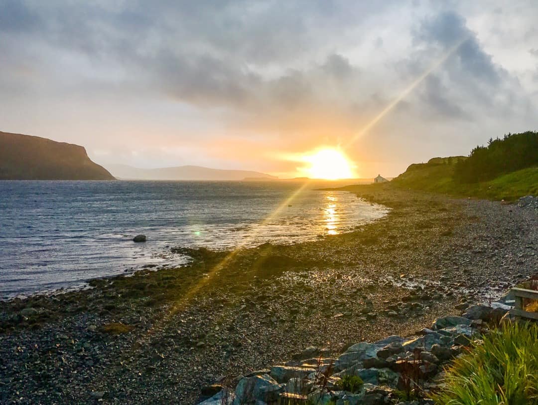 The sun breaks through clouds as it sets over Loch Bay on Skye.