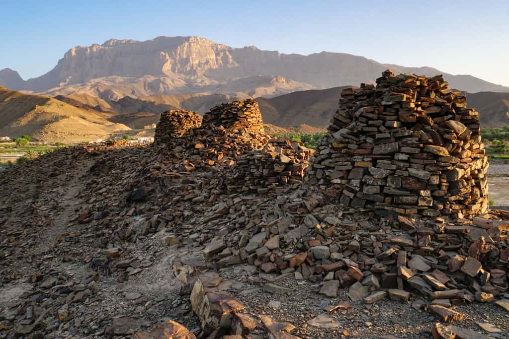 Oman photography – sunset slowly turns tombs of Al Ayn golden as the mountain backdrop enjoys the last light of the day.