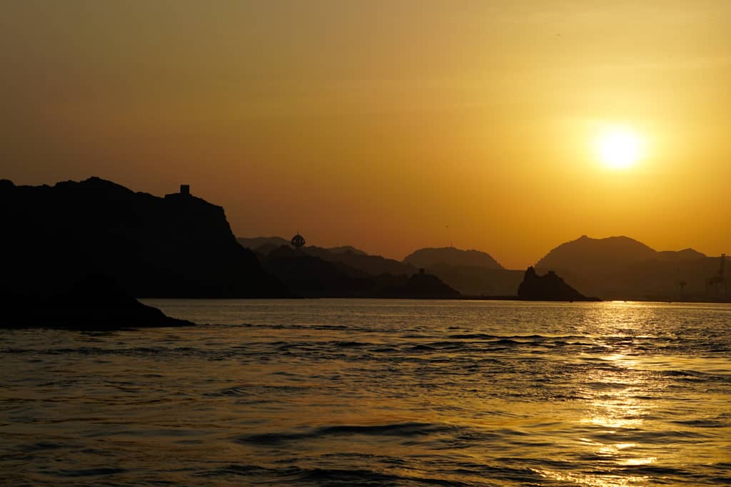 Oman photo gallery – a glorious sunset during a dhow cruise along the Gulf of Oman looking back towards a mountainous landscape dotted with fortresses.