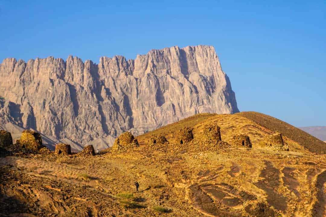 Late afternoon sun lights up the ancient tombs of Al-Ayn and imposing Jebel Misht mountain range, one of our Oman highlights.