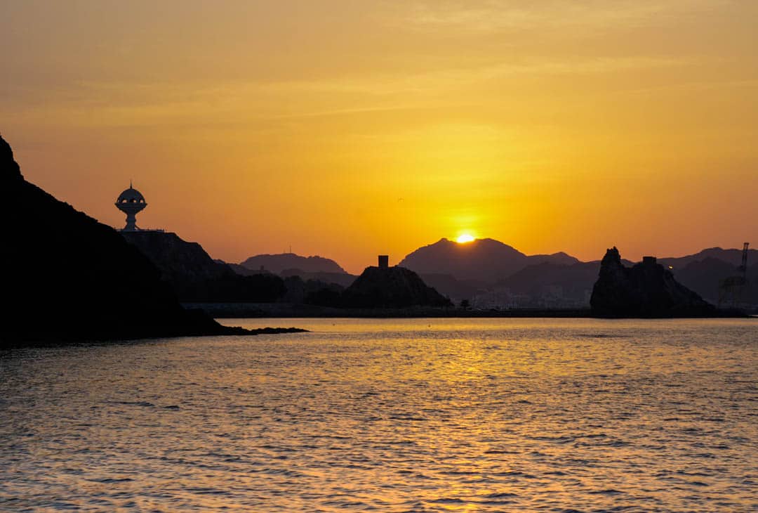 The sky turns deep orange as the sun sets behind a mountain during a dhow boat cruise, a must for any Oman tour.