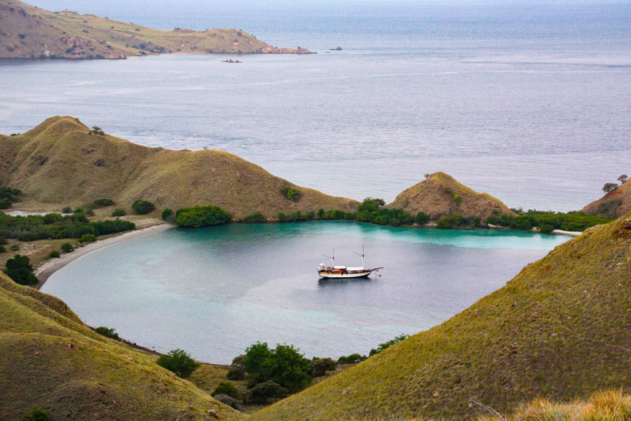 Hilltop view of Wunderpus liveaboard in a secluded curved bay early in the morning while diving Komodo National Park.