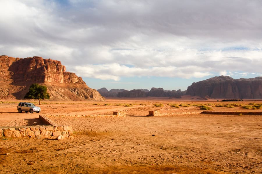 A 4WD sits in a rusty-coloured desert with huge cliffs and rocky rises in the background.