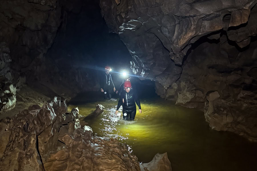 People in wetsuits wearing head torches wade through water in a cave in New Zealand, one of the world's top adventure destinations.
