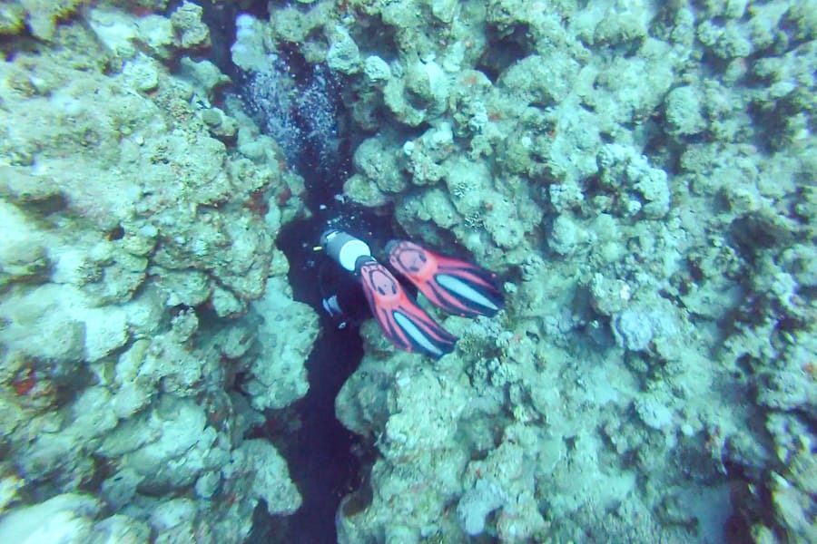 A diver disappears into a narrow crevasse at The Canyon dive site in the Red Sea.