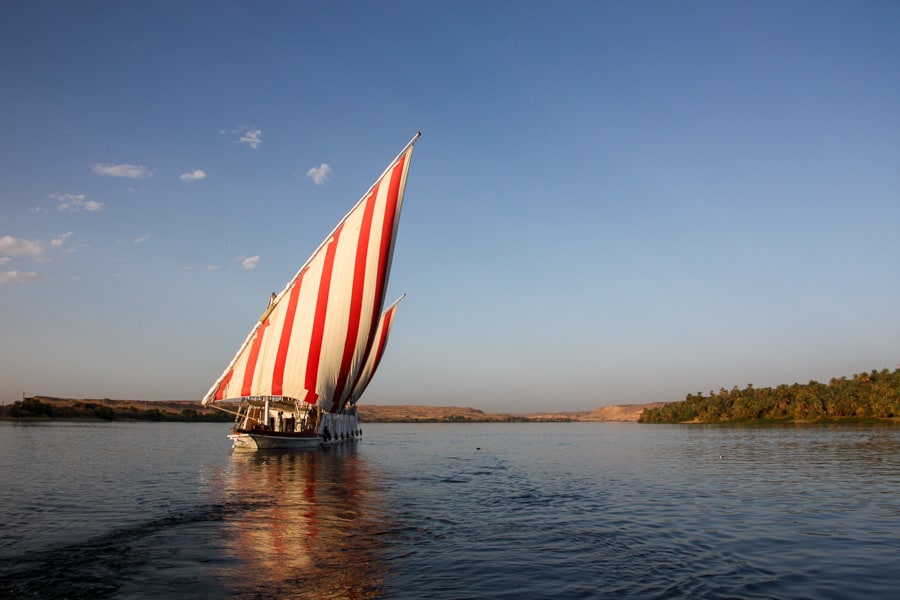 Red-and-white striped sails billow on a traditional dahabiya boat on the Nile. 