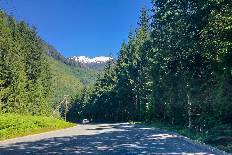 A snow-capped mountain rises above the road on Vancouver Island, Canada.