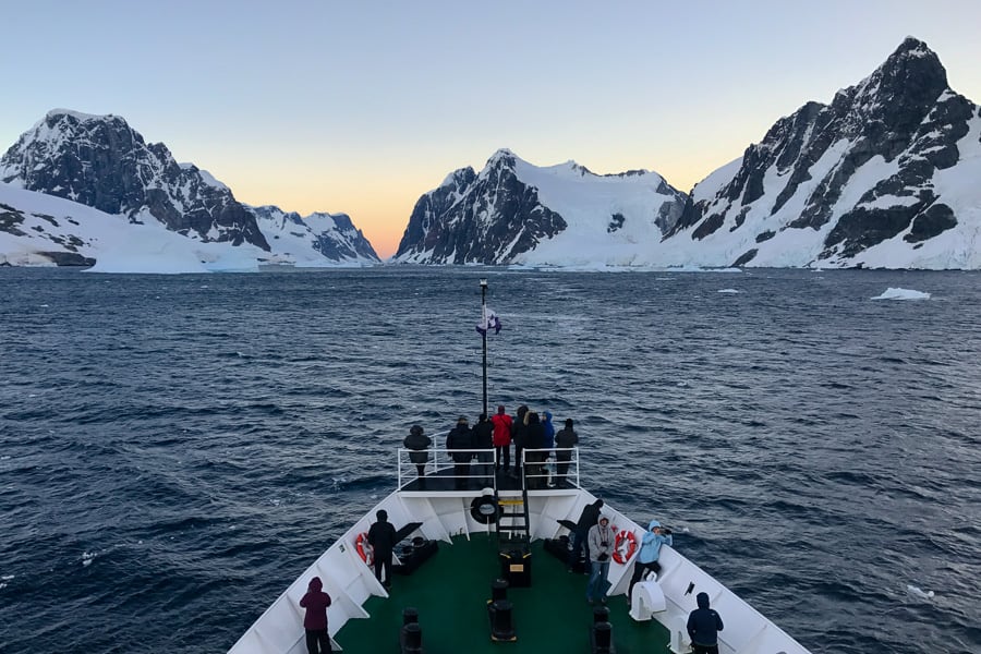Expedition ship cruises towards snow capped mountains in Antarctica.