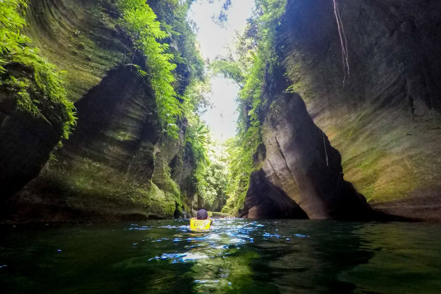 A person floats through a river gorge between cliffs on one of the Pacific Islands' greatest adventures.