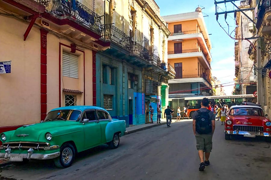 A man walks between two vintage cars on a Havana street on Day 1 of our Cuba travel itinerary.