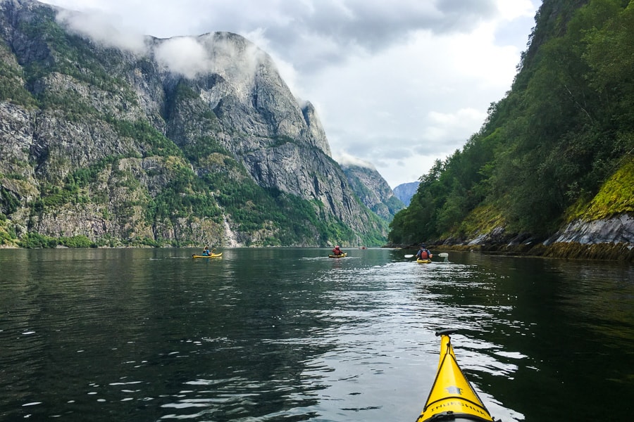 Kayakers paddle between high, mist-shrouded cliffs in Norway.