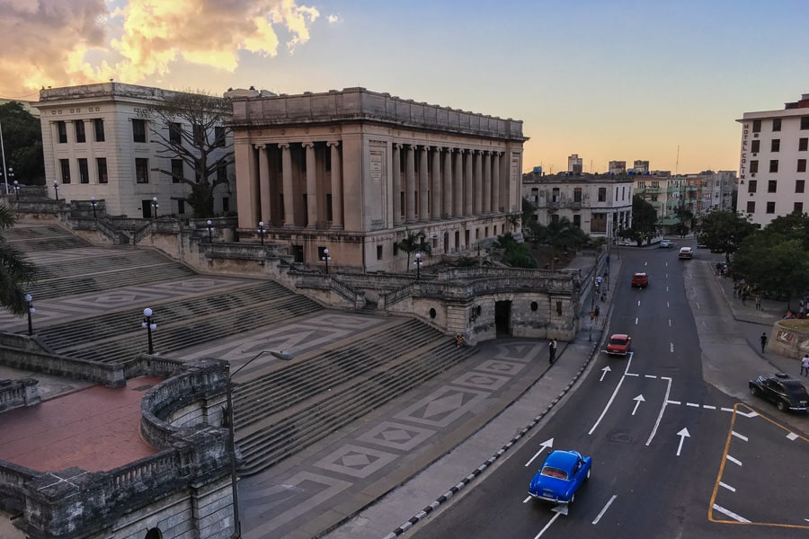 Road Trip List: Blue vintage car cruises past the University of Havana, Cuba.
