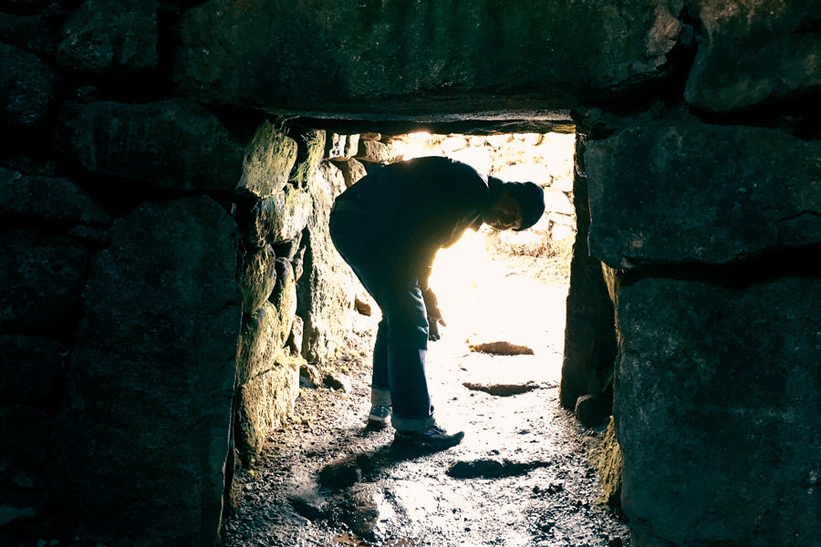A person leans over to fit inside a stone tunnel at Carn Euny on a London to Cornwall road trip.