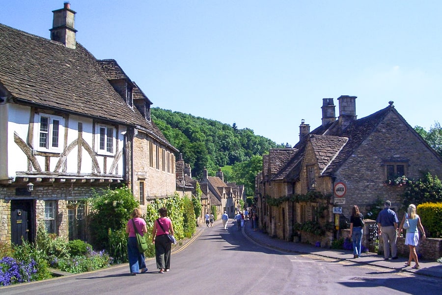 People walking along a medieval village street in the Cotswolds on a South West England road trip.