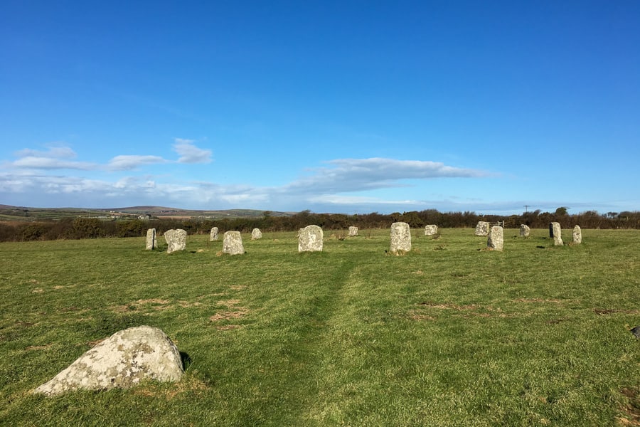 Places to visit in south west England: a circle of ancient stones stand in a field under a blue sky.