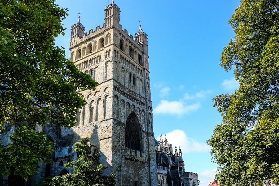 The bell tower of Exeter Cathedral surrounded by trees can be seen when you road trip south west England.