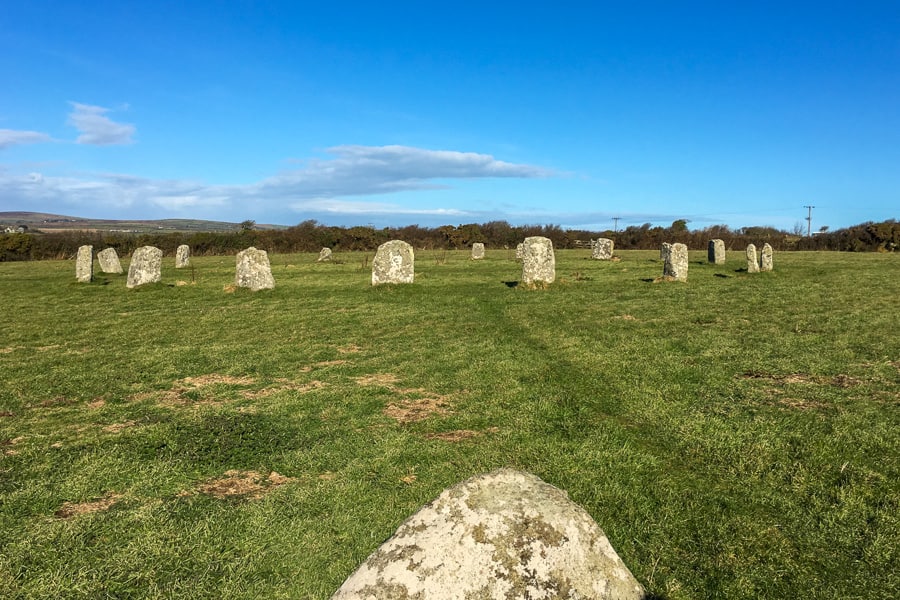 A circle of stones in a field with a single stone in the foreground, one of our favourite places to visit in south west England. 