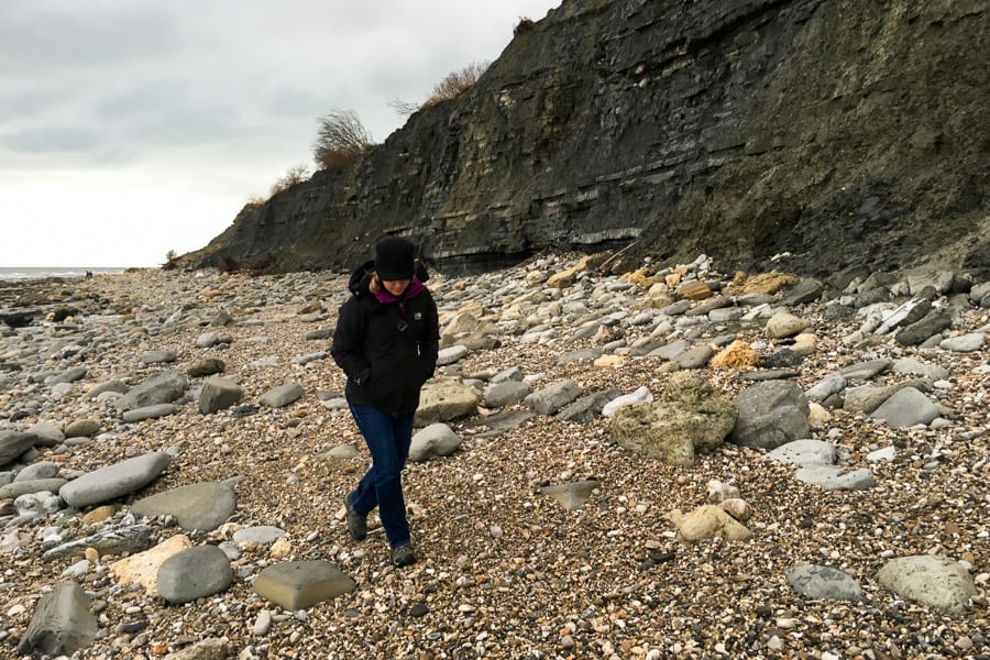 A person walking on the rocky shore of Monmouth Beach looking for fossils. 