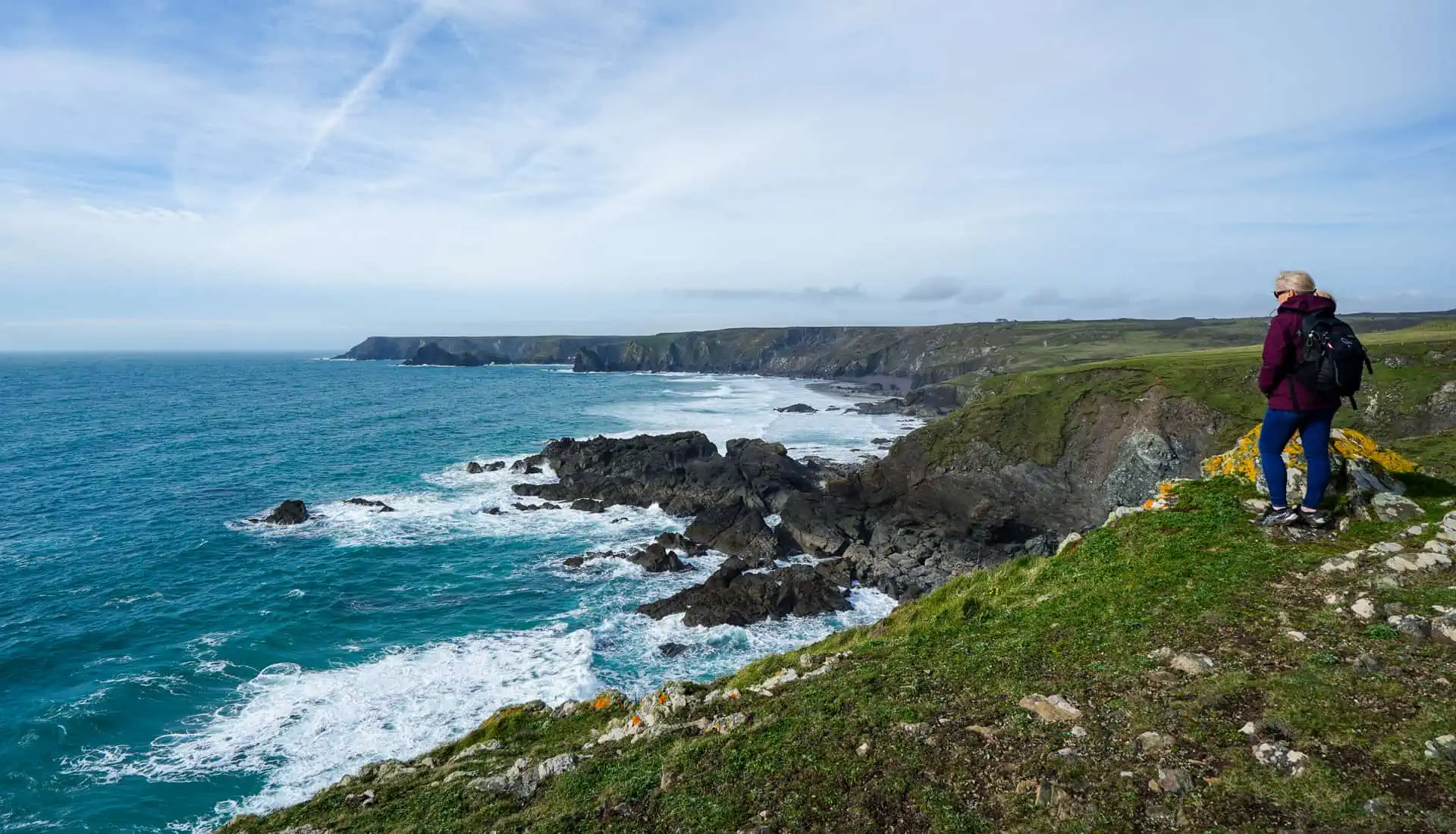 A person looks out over cliffs and ocean of the Cornwall coastline.
