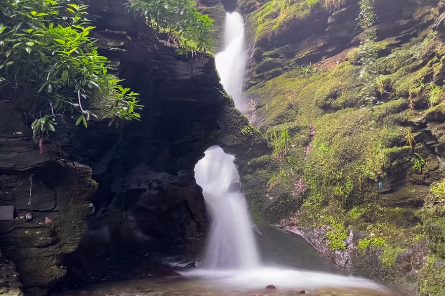 A waterfall cascades down a rocky cliff and through a hole surrounded by green vegetation. 