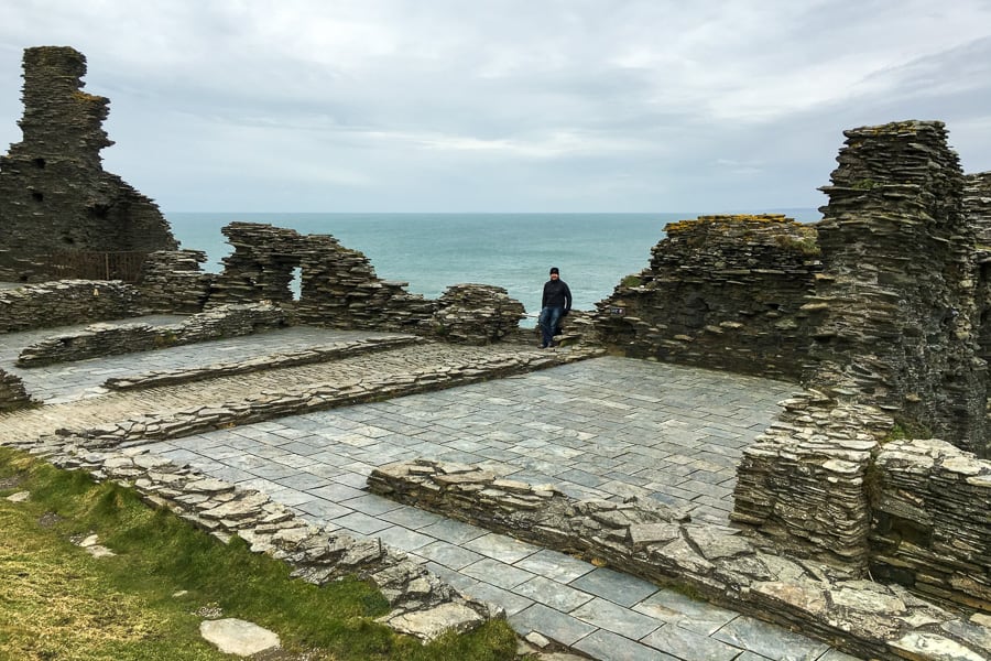 John sits among the slate ruins of Tintagel Castle above the sea.