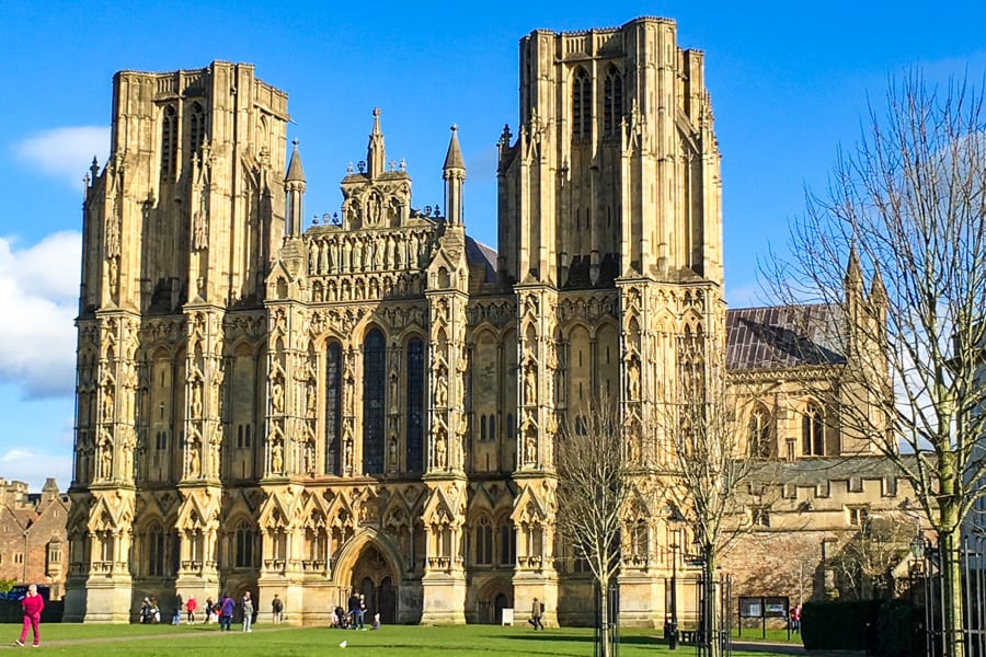 The intricate stone façade of Wells Cathedral with people walking in front.