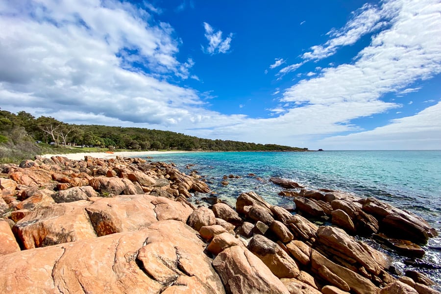 Looking out over red rocks, green trees, white sand and aqua sea at Meelup Beach, one of many beautiful beaches in Western Australia.