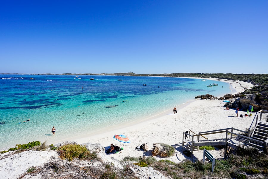 People relax on white sand lapped by cyan water on one of the spectacular Western Australia beaches of Rottnest Island.