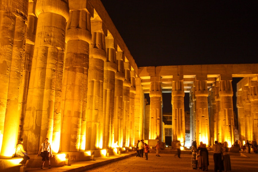 Rows of lotus-topped columns are lit up with spotlights under a dark sky at Luxor Temple.