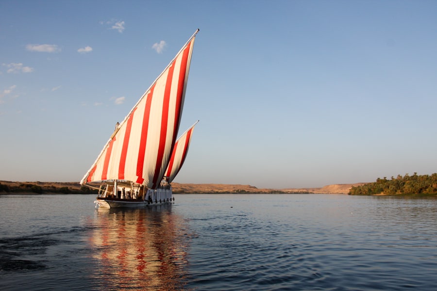 Red and white sails billow above a white dahabiya boat, a must-do on our 2 week Egypt itinerary. 