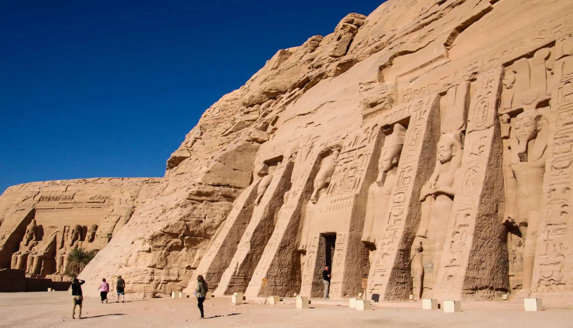 Egypt Highlights - Colossal statues stand guard at the Temple of Hathor in Abu Simbel, with the Temple of Ramses II in the background.