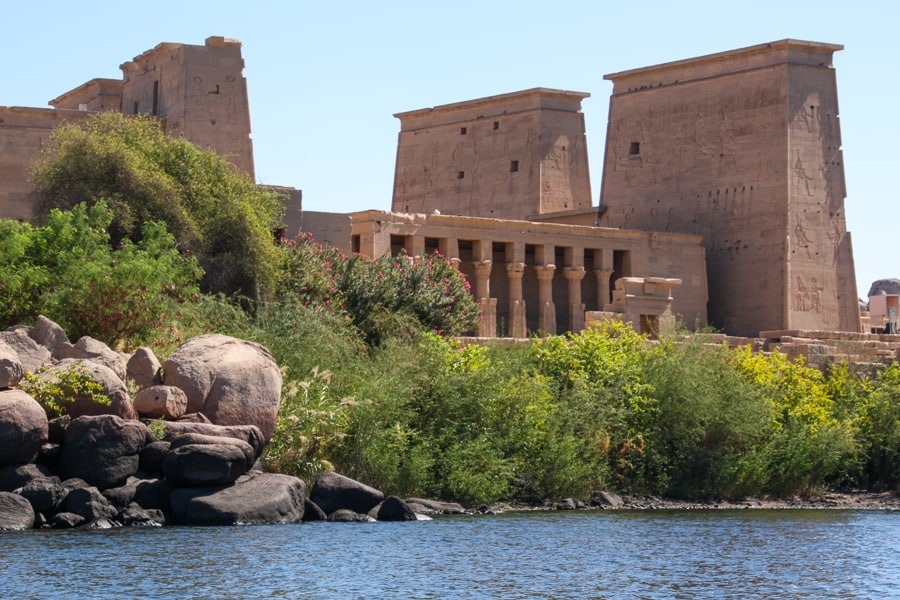 Egypt highlights - The huge pink stone pylons and columns of Philae Temple rise above green foliage and water.