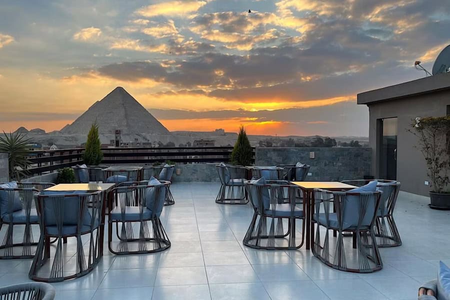 Chairs and tables on a rooftop looking towards a pyramid of Giza.