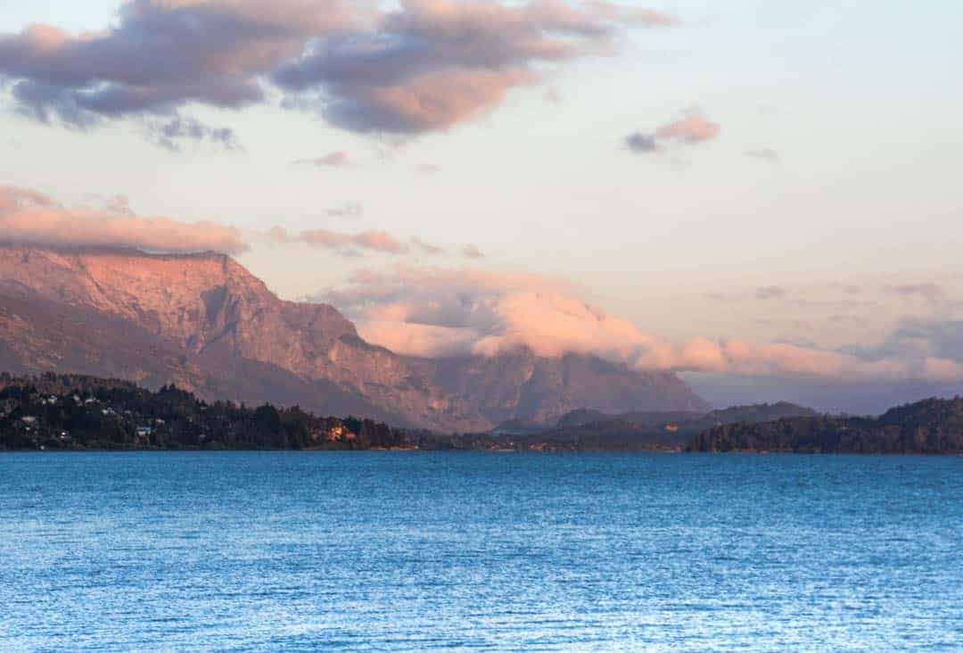 Sunrise lights the mountains behind the lake and turns the clouds pink, a real treat for early risers visiting Bariloche