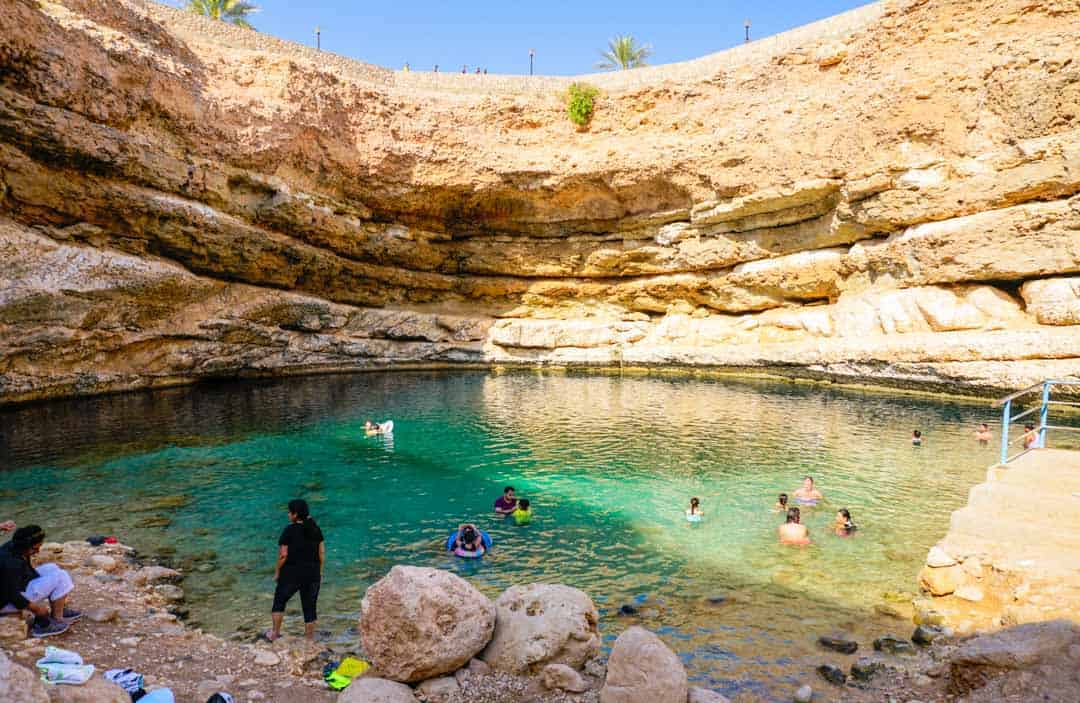 Sun pours into Bimmah Sinkhole illuminating the swimmers. For most people a visit here is one of their Oman Highlights.