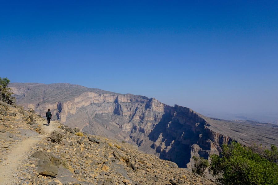 A hiker walks along the Balcony Trail overlooking a canyon and mountain landscape - one of our personal highlights of Oman.