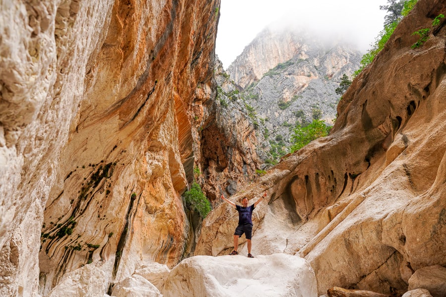 Sheer limestone walls engulf a hiker at Gola Su Gorropu, a must-do hike to include on your Sardinia trip.
