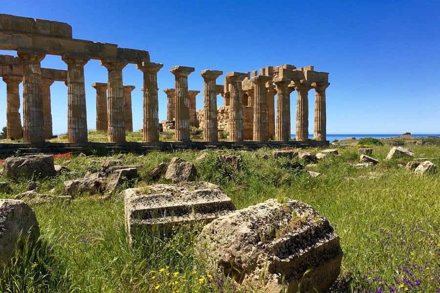 A favourite place on our Sicily road trip – the ruins of one of the Selinunte temples rises above tall green grass backed by blue sea. 