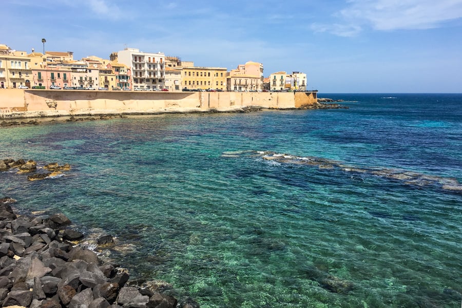 Teal-coloured water laps at the yellow city sea walls of ancient Ortigia in Syracuse.  